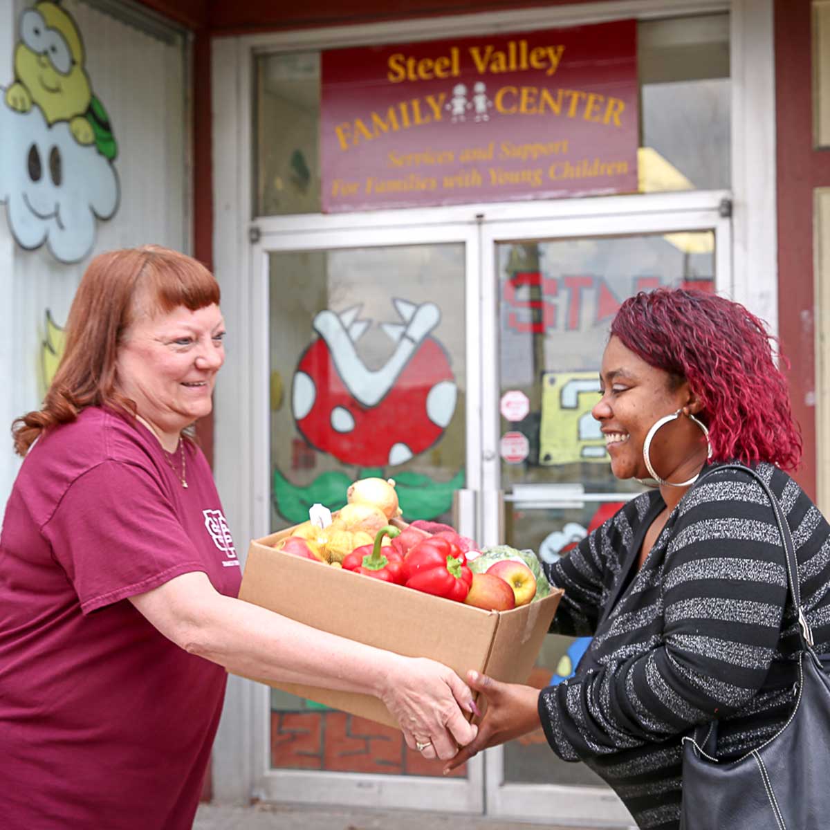 Two women carrying a box of vegatables